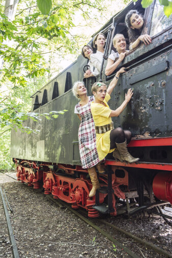 Sechs Frauen sitzen im und hängen an einer Lokomotive.
