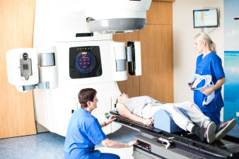 Zwei Krankenschwestern betreuen eine liegende Person bei der Bestrahlung.