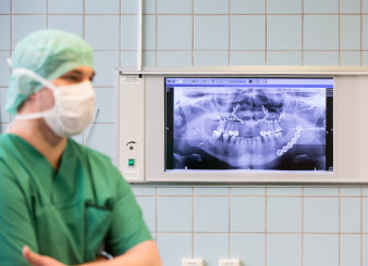 Foto: MKG © Helios Kliniken GmbH Arzt mit Monitor, auf dem ein Röntgenbild des Kiefers abgebildet ist