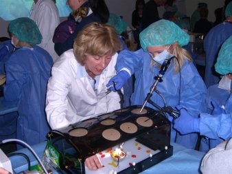 Foto: Minimalinvasive Chirurgie © Helios Kliniken GmbH Ein Kind in OP-Kleidung mit Unterstützung einer Ärtzin probiert mit minimalinvasiver Technik Gummibärchen zu fassen.