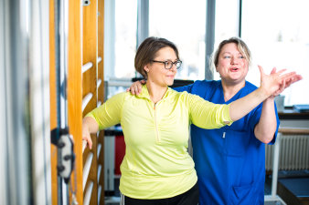 Foto: Physiotherapie © Helios Kliniken GmbH Physiotherapeut unterstützt, zeigt der Patientin die Bewegung