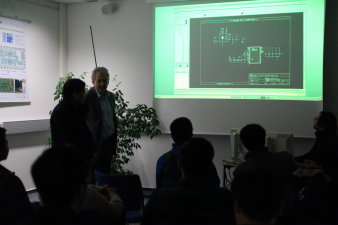 Foto: IMMS – Vorträge © Beate Hövelmans Gäste sitzen im Vortragsraum und schauen auf die Chip-Entwurfs-Software, die gerade vorgestellt und per Beamer an die Wand projiziert wird.