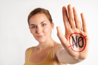 Foto: Sexismus am Arbeitsplatz © Colourbox.de Eine junge Frau im Shirt, eine Hand mit durchgestrichenem "NO" auf Handfläsche nach vorne ausgestreckt