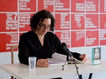 Foto: Anke Stiller performt „Miranda“ © Philipp Valenta eine Frau liest vor ainem Mikrofon aus einem Buch