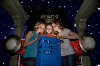 drei Mädchen schauen in eine dunkelblaue Papiertüte mit dem schwarzen Schriftzug „Abendstund hat Licht im Kopf“