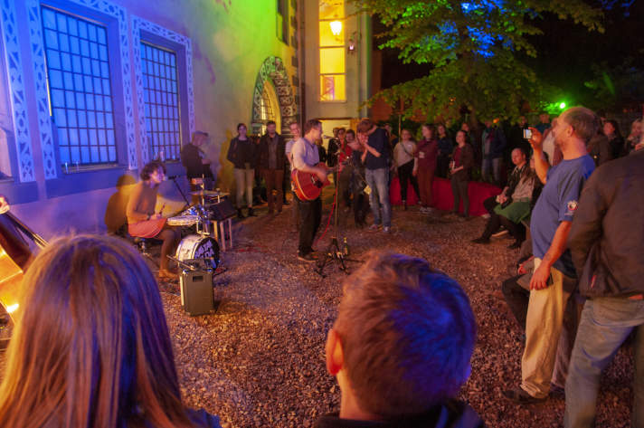 Ein beleuchteter Hof mit Musikern und Publikum