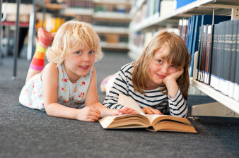 Foto: Kinder in der Universitätsbibliothek Erfurt © Universität Erfurt Zwei Kinder auf dem Bauch vor einem Buch liegend
