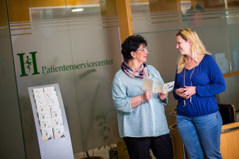 Foto: Patientenservicecenter © Helios Kliniken GmbH zwei stehende Frauen mi Flyer