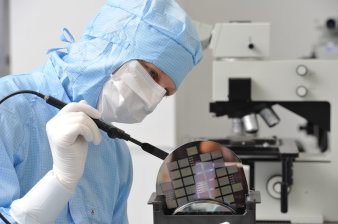 Foto: Mikrotechnologin © Barbara Neumann Mitarbeiterin im Reinraumanzug hält einen Siliziumwafer mit der Vakuumpinzette