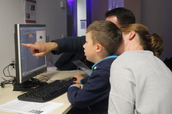 Foto: Selber machen lassen – Programmieren für Kinder © IMMS / Beate Hövelmans Ein Junge sitzt mit seinen Eltern vor einem Computer und programmiert in einer grafischen Programmierumgebung.