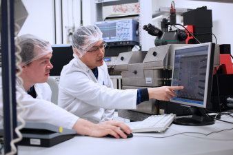 Foto: Mikroelektronik auf dem Prüfstand © IMMS / Beate Hövelmans Zwei Forscher des IMMS vor einem Wafer-Prober und einem Bildschirm, der die Testergebnisse anzeigt.