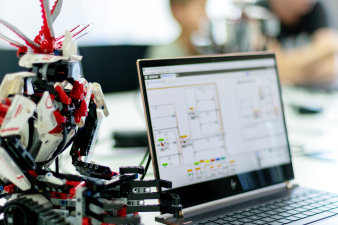 Foto: Spaß am Programmieren © Rewe Digital bunter Roboter und aufgeklappter Notebook mit Schaltplan auf dem Display