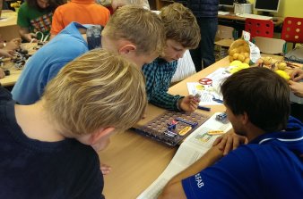Foto: Spannende Experimente - Mitmachaktion © Antje Geiger Schüler und Auszubildende sitzen an einem Tisch an den verschiedene Experimente aufgebaut sind.