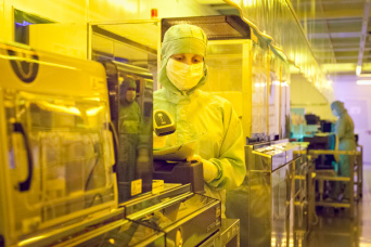 Foto: Mitarbeiterin im Bereich Fotolithografie im Reinraum der X-FAB © Andreas Hultsch Mitarbeiterin mit Scanner in der Hand im Bereich Fotolithografie, in dem gelbes Licht herrscht, im Reinraum der X-FAB